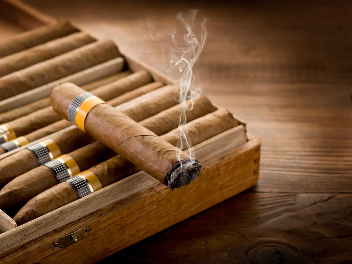 Smoking cuban cigar over box  on wood background